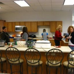 Five women in an office kitchen, preparing food for an office party.