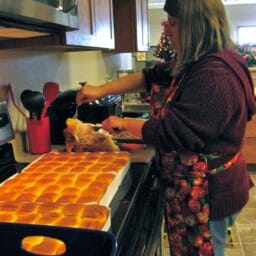 A woman carving a turkey in an office kitchen, with browned rolls nearby.
