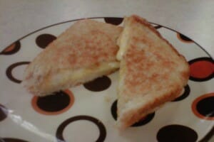 Two halves of a grilled cheese sandwich on a plate with orange and brown circles.