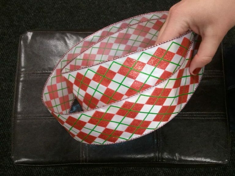 A woman's hand holding a red, green, and white plaid ribbon.