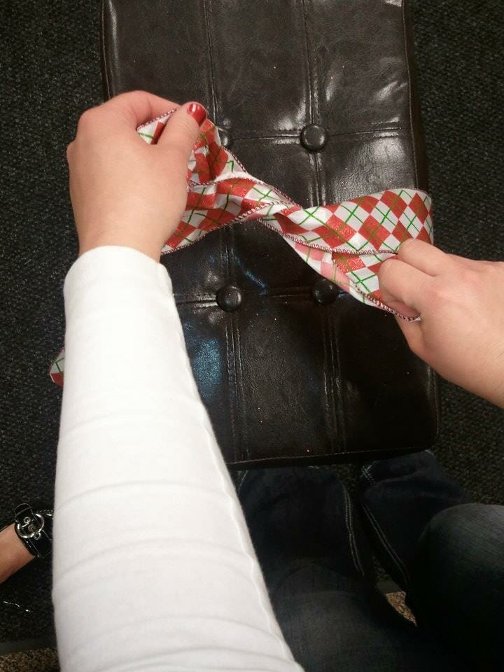 A woman's hands tying a length of red, green, and white plaid ribbon around a brown leather stool.