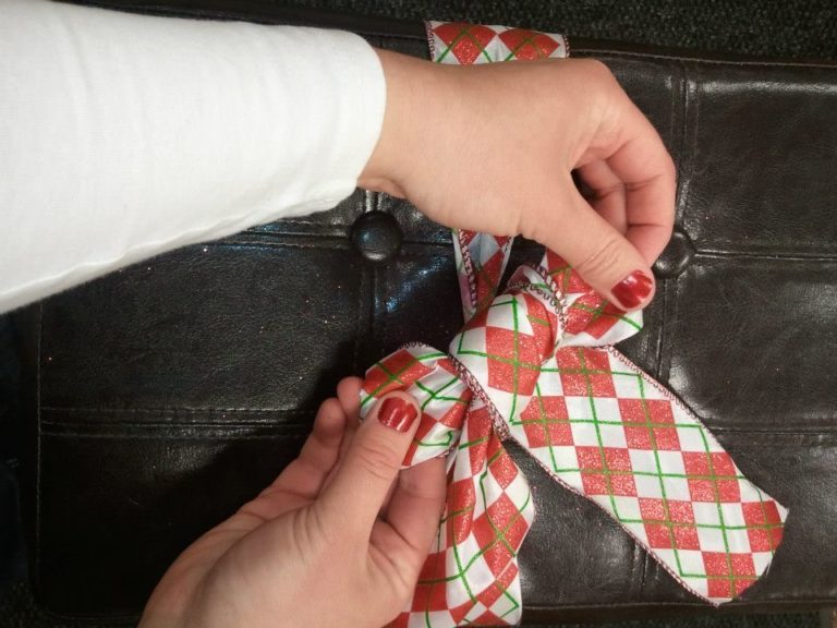 A woman's hands tying a red, green, and white plaid ribbon bow around a brown leather stool.