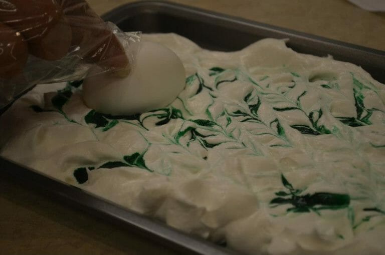 A dozen white eggs in shells placed in a muffin pan that is on a rack in an oven.