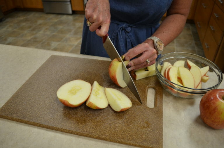 A woman cutting apple slices on a brown cutting board with a red-handled knife.