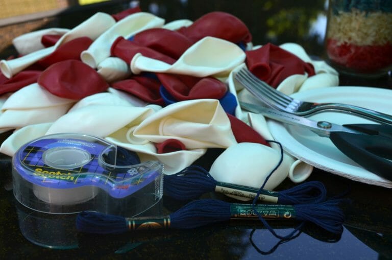A black counter piled with red, white, and blue deflated balloons, tape, scissors, blue floss, and a fork.