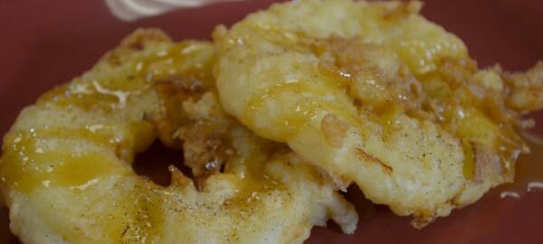 Two deep fried apple rings on a red plate, topped with cinnamon and sugar.