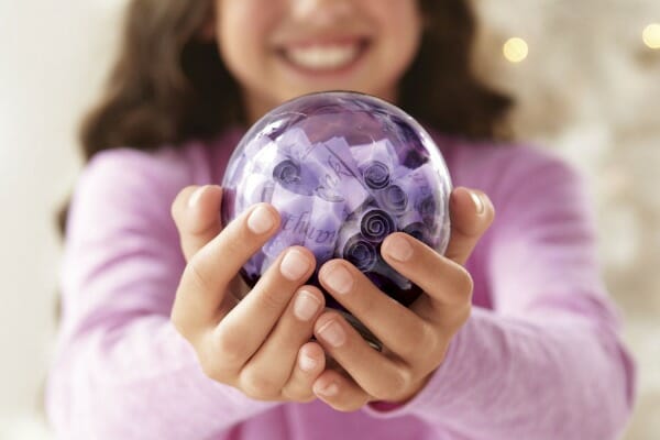 A girl in a lavender top holding a purple ornament filled with rolled strips of paper.