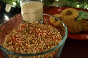 A clear glass bowl of Reindeer Food, next to a red plate of cookies and a glass of milk.