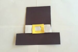 A simple Pilgrim hat shape made from black paper with a white paper band and a yellow paper buckle.