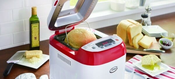 Ginny's red and white bread machine with a loaf of bread in the cooker, and one on a counter with cut slices.