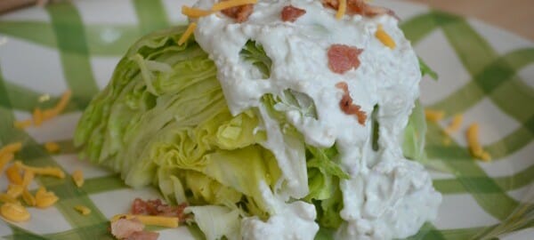 A green and white plate with a lettuce wedge topped with Bacon Bleu Cheese Dressing.