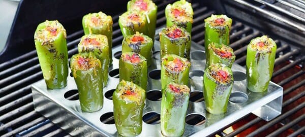 Several Jalapeno Poppers upright in a metal pan with holes, placed on a flaming grill.