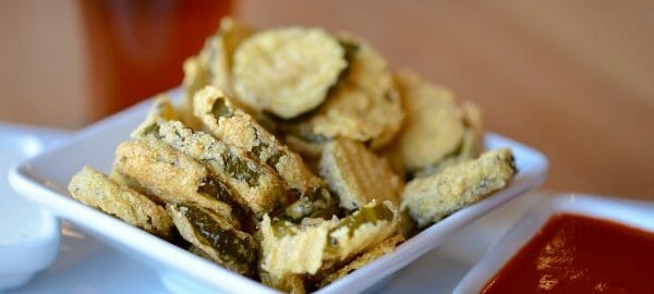 A square white plate filled with deep fried pickles.