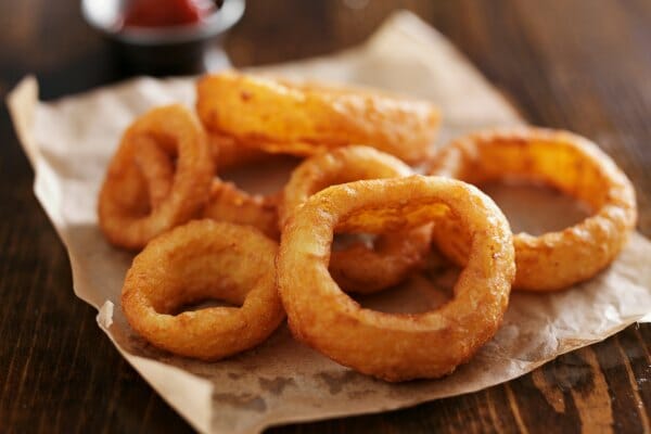A pile of fried onion rings draining on brown parchment paper.