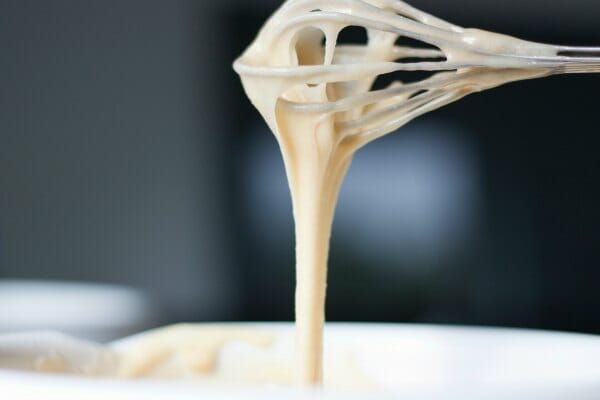 A whisk with dripping creamy batter, poised above a bowl.