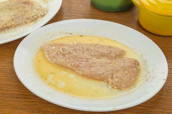 A raw chicken breast in an egg filled bowl, waiting to be dredged in a coating, before deep frying.