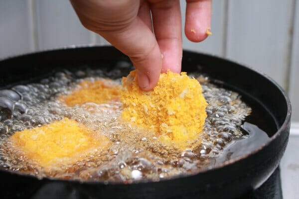 A hand slowly lowering a breaded piece of food into a frying pan filled with bubbling hot oil.