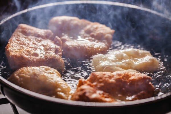 A black frying pan filled with pork chops sizzling in smoking, bubbling oil.