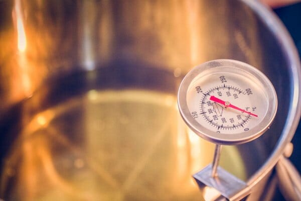 A thermometer hooked on a stainless steel pot, checking the temperature of oil for frying.