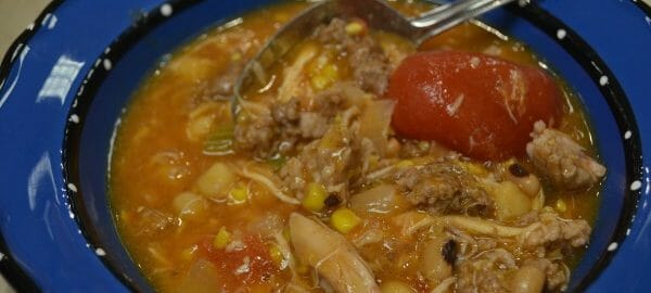 Close-up of an individual serving of Brunswick stew in a bright blue bowl, with a spoon.