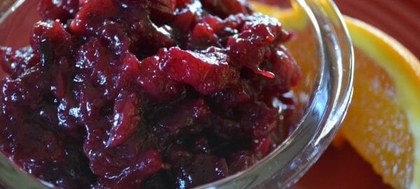 Close-up of a clear glass ramekin filled with Cranberry Sauce with Orange, served with an orange slice.