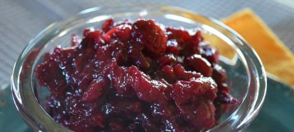 Close-up of a clear glass ramekin filled with Cranberry Sauce with Pineapple, placed on a blue plate.