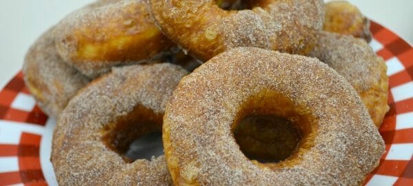 A red and white plate stacked with homemade biscuit donuts dipped in sugar.