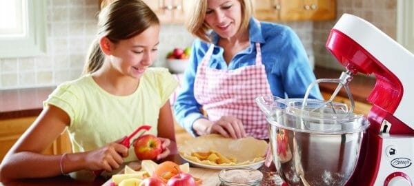 A woman and her daughter peeling apples for a pie, with a Ginny's brand stand mixer on the kitchen counter.