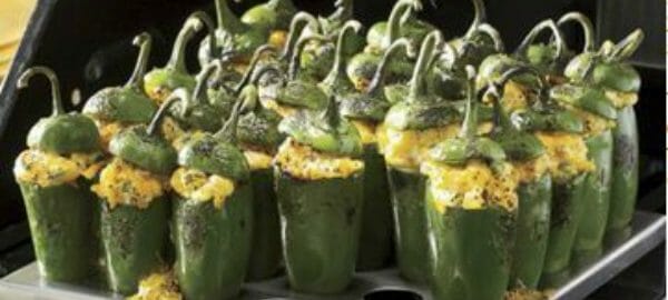 Several Jalapeno Poppers upright in a metal pan with holes, placed on a grill.