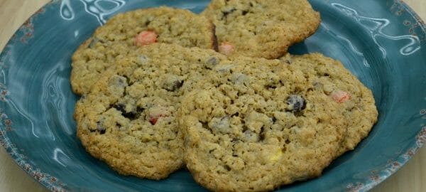 A blue plate with four Monster Cookies made with oatmeal, chocolate chips, and raisins.