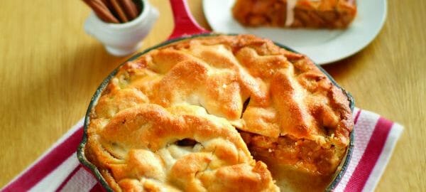 A red skillet filled with Skillet Apple Pie, with a sliced removed to a white plate, topped with a scoop of ice cream.
