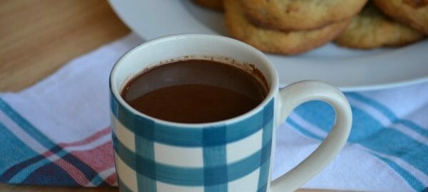 A blue and white mug filled with Slow Cooker Bacon Hazelnut Hot Chocolate, next to a plate filled with cookies.