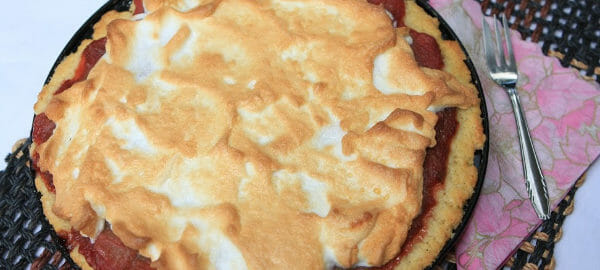 A Rhubarb Custard Pie topped with meringue, and placed on a brown woven table runner.