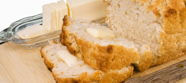 A loaf and two buttered slices of Beer Bread, next to a filled butter dish.