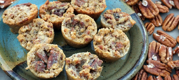 A multicolor blue plate with Pecan Pie Muffins, surrounded by whole pecans.