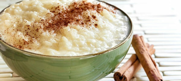 A green bowl filled with rice pudding topped with cinnamon, with two cinnamon sticks nearby.