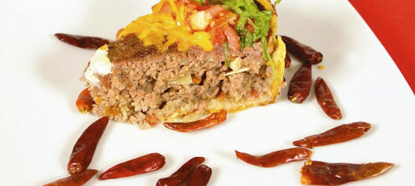 A square white plate with a serving of Taco Pie, surrounded by dried jalapeno peppers.