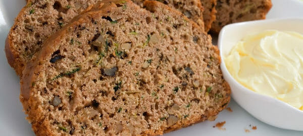 Close-up of slices of Zucchini Bread on a white plate, with a ramekin of whipped butter.