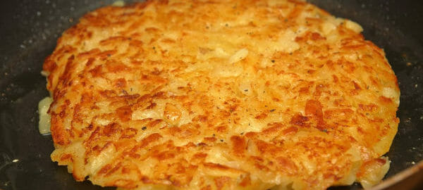 Close-up of golden Swiss Roesti Potatoes inside a black skillet.