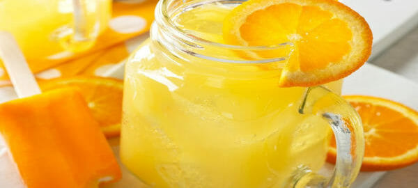 A Mason jar mug filled with Creamsicle Ice and a sliced orange garnish, next to an Orange Creamsicle ice cream bar.
