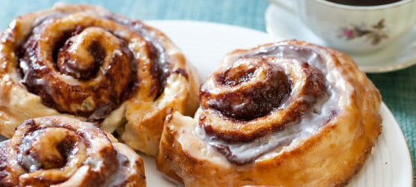 white plate with four iced cinnamon rolls, and tea in a floral coffee cup.
