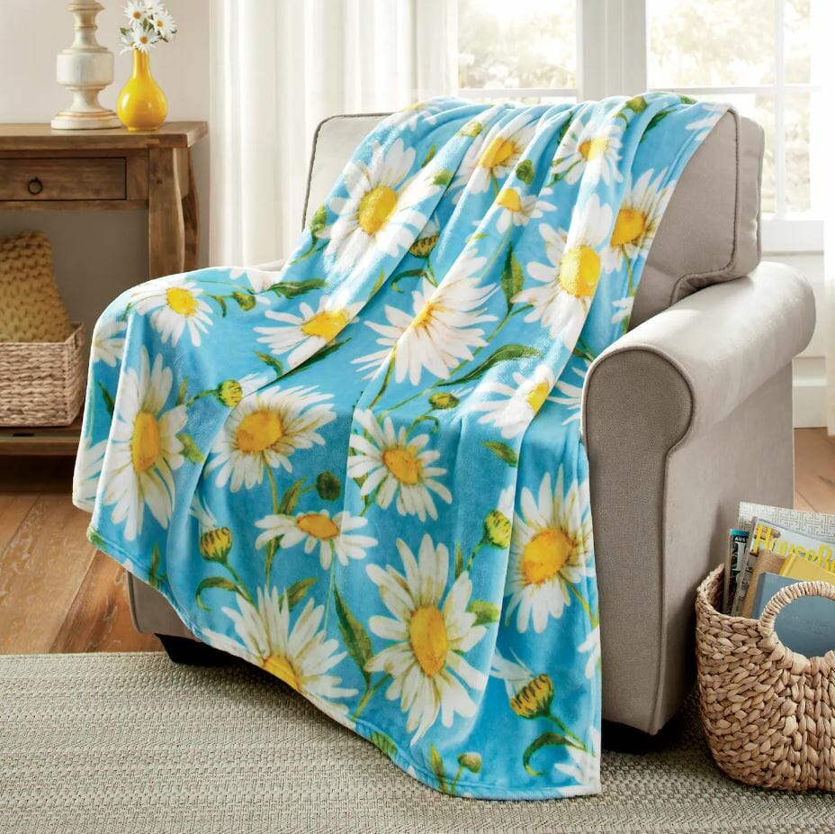 Cozy blue blanket adorned with daisies drapes over a light gray armchair in a bright, inviting living space.