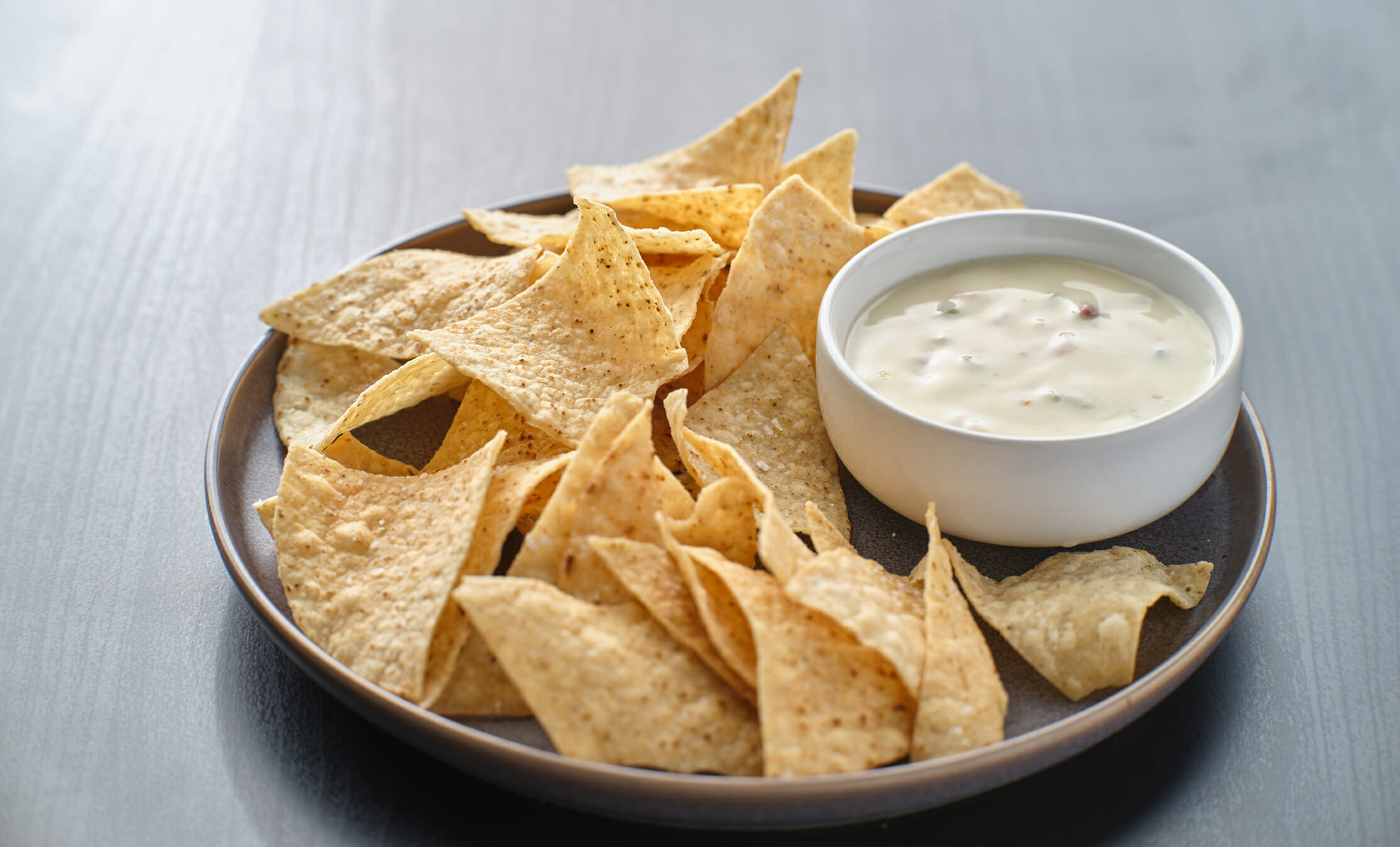 Crispy tortilla chips arranged on a plate, accompanied by a small bowl of creamy dip.