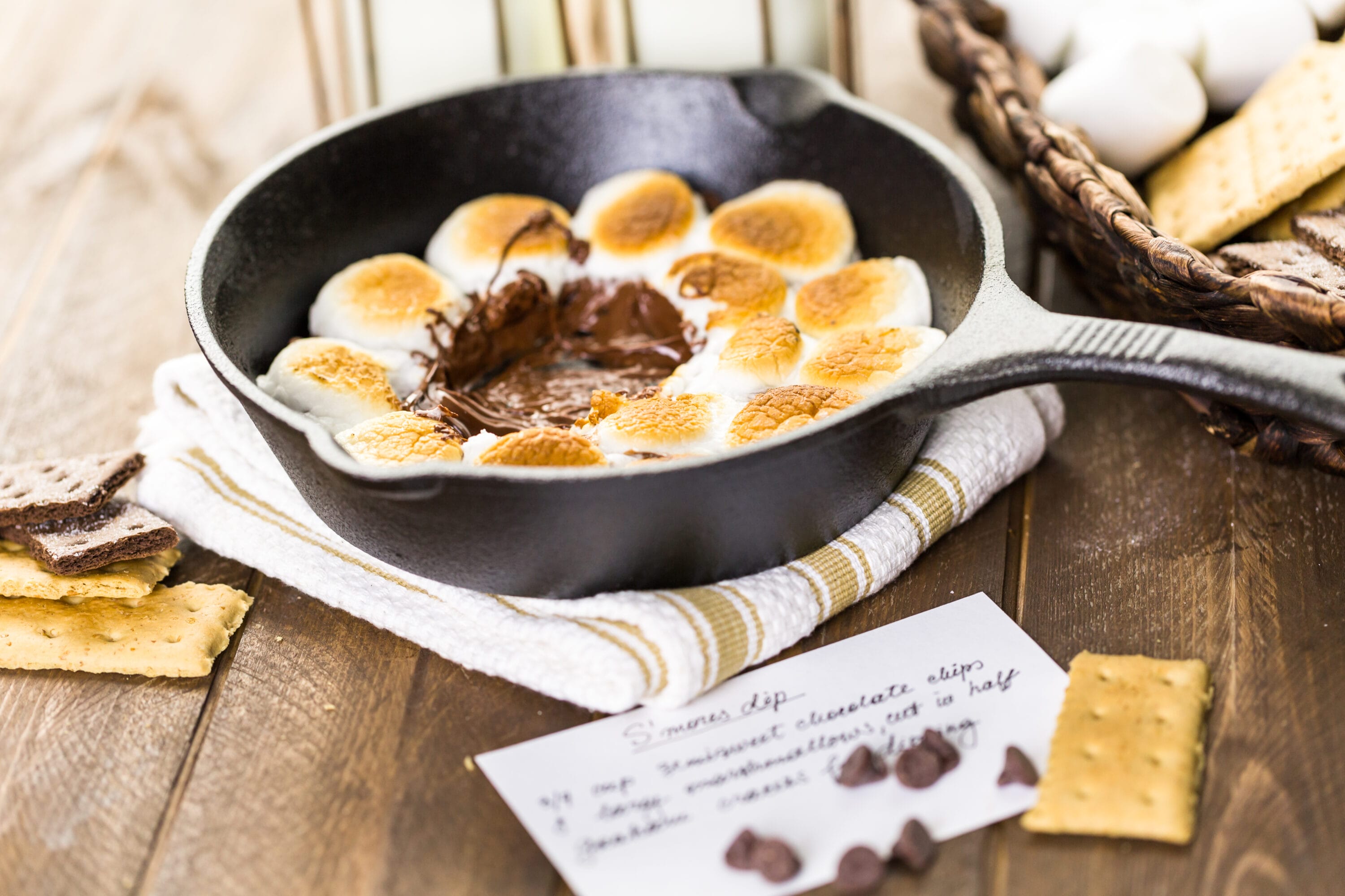 Cast Iron skillet resting on a folded towel containing roasted marshmallows with melted chocolate