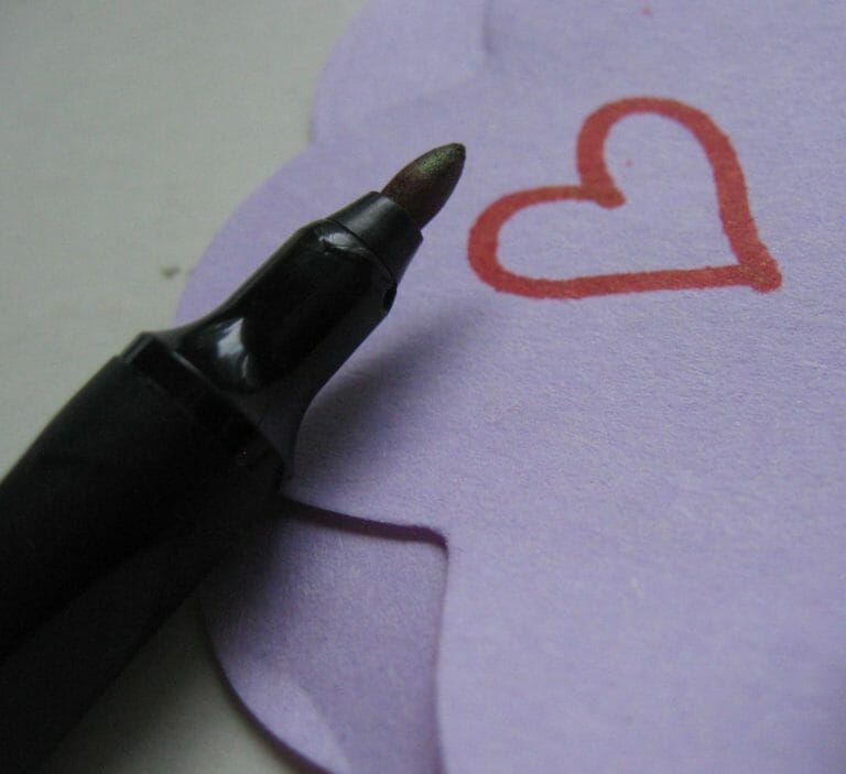 A black pen by a red heart drawn on heart-shaped lavender paper.