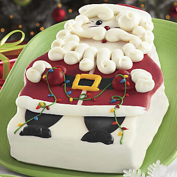 A decorated cake of Santa in red a red suit holding Christmas lights.