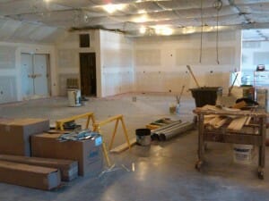 Interior of a business's large room with construction materials and taped walls, waiting to be painted.