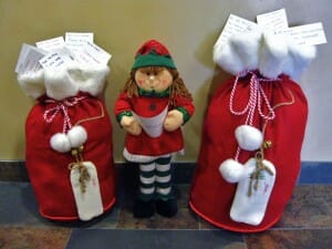Santa's girl Elf standing by two red and white mail bags filled with letters to Santa.