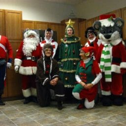 Eight people in an office wearing Christmas costumes, including Chris Mouse, Santa, an Elf and a cookie.