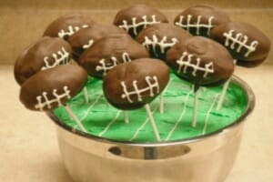 Cake pops in the shape of footballs stuck in a field of green frosting.